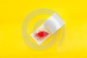 Proctology concept with toilet paper roll and red feather on yellow background top view