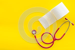 Proctology concept with toilet paper roll and stethoscope on yellow background top view space for text