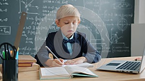 Prodigy kid taking notes in university classroom with chalkboard in background