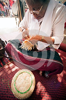 Product by hand made, hand of Senior Ethnic woman holds took bamboo stripes to weave into different.