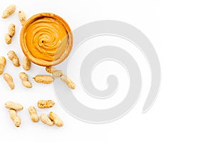 Product for hearty breakfast. High-calorie product. Peanut butter in bowl near nuts in shell on white background top