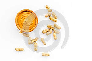 Product for hearty breakfast. High-calorie product. Peanut butter in bowl near nuts in shell on white background top