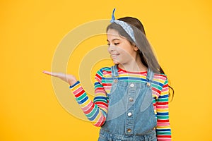 Product presentation. Kid happy smiling face show something on open palm copy space yellow background. Girl demonstrate