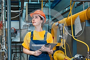 Production inspection. A young engineer in a uniform and a protective helmet, holding a tablet in his hands and