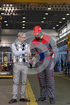 Production Manager With Digital Tablet Giving Instructions To Worker In Protective Workwear