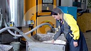 Production plant worker works with loader hose vacuum sucking white virgin plastic granules from tank in factory