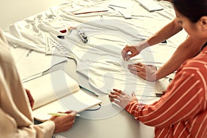 Production process. Male hands working with sketches or patterns at studio and preparing fabric. Group of millennials