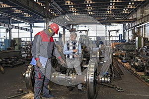 Production Supervisor Talking To African American Worker Next To Train Wheels At Train Factory