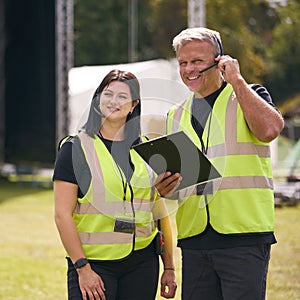 Production Team Talking On Headsets Setting Up Outdoor Stage For Music Festival Or Concert