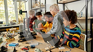 Productivity is the best for us. Group of smart kids listening to their male teacher while looking at 3d printer and