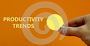 Productivity trends symbol. Businessman hand holding light bulb. Words `Productivity trends`. Beautiful orange background, copy