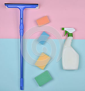 Products for cleaning glass windows. Sponges, window mop, sprinkler cleanser on a blue pink pastel background.