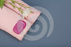 Products for facial and body care. Soft terry towels with soap and flower on gray background. Spa and bodycare concept.