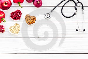 Products good for heart and blood vessels. Vegetables, fruits, nuts in heart shaped bowl near stethoscope on white