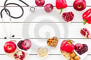 Products good for heart and blood vessels. Vegetables, fruits, nuts in heart shaped bowl near stethoscope on white