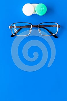 Products help see better. Glasses with transparent optical lenses and eye lenses on blue background top view copy space