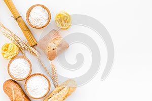 Products made of wheat flour. White flour in bowl, wheat ears, fresh bread and raw pasta on white background top view