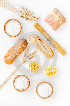 Products made of wheat flour. White flour in bowl, wheat ears, fresh bread and raw pasta on white background top view