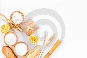 Products made of wheat flour. White flour in bowl, wheat ears, fresh bread and raw pasta on white background top view