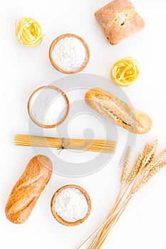 Products made of wheat flour. White flour in bowl, wheat ears, fresh bread and raw pasta on white background top view