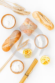 Products made of wheat flour. White flour in bowl, wheat ears, fresh bread and raw pasta on white background top view