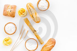 Products made of wheat flour. White flour in bowl, wheat ears, fresh bread and raw pasta on white background top view