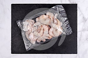 Products in vacuum packaging on black slate board. Frozen shrimps, vacuum sealed food ready for sous vide cooking. Sous-vide, new