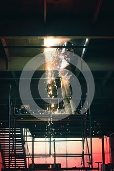Profesional welder in protective uniform and mask welding metal construction in the industrial object photo