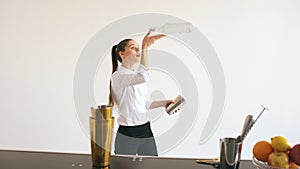 Professinal bartender girl juggling bottles and shaking cocktail at mobile bar table on white background