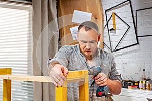 Profession, carpentry, woodwork and people concept - carpenter with electric drill drilling wood plank at workshop