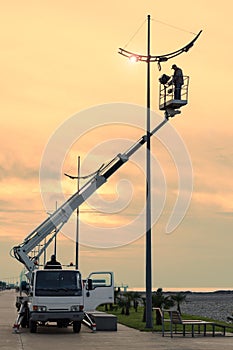 Profession repair and maintenance of street lamps - car with crane lifted an electrician to replace bulbs at sunset in evening.