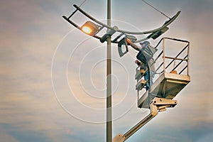Profession repair and maintenance of street lamps - crane lifted an electrician to replace bulbs at sunset in evening.