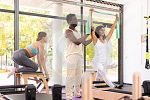 Professional African American man instructor controlling woman exercising with resistance bands