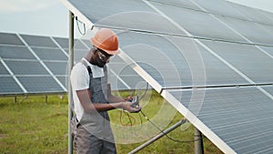 Professional african engineer in helmet and uniform using multimeter for measuring amperage in solar panels. Concept of