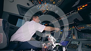 Professional aiplane pilot is turning indicators on a cockpit cabin flight deck.