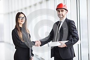 Professional architect and businesswoman handshake against panoramic window in office.