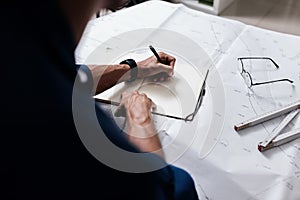 Professional architect makes notes in a notebook on a table with a drawing and ruler