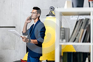 Professional architect talking on the phone in a room with a stylish interior with sofa with pillows and bookshelves in