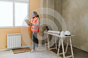 Professional architect woman in construction site talking on mobile phone holding blueprints