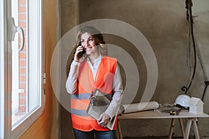 Professional architect woman in construction site talking on mobile phone holding blueprints