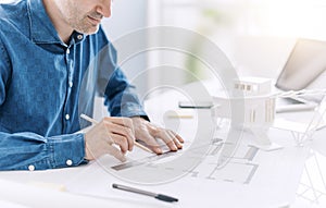 Professional architect working at office desk, he is drawing and making measurements on a project blueprint, design and