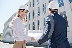 Professional architects in hardhats holding blueprint while working at construction site