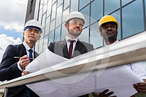 Professional architects in helmets working with blueprint outside modern building