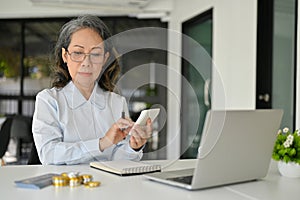 Professional Asian aged female accountant using calculator, managing financial sales accounts