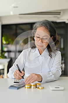 Professional Asian aged female accountant using calculator, managing financial sales accounts
