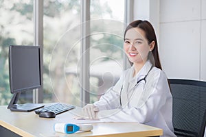 Professional Asian beautiful young smiling female doctor wears rubber glove sitting looking at camera while waiting for patient