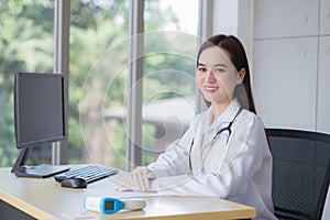 Professional Asian beautiful young smiling female doctor wears rubber glove sitting while waiting for patient examination in