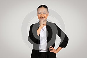 Professional Asian businesswoman with a secretive expression placing a finger to her lips