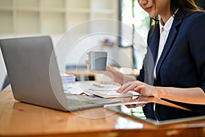 Professional Asian businesswoman sipping coffee while working at her desk, using calculator