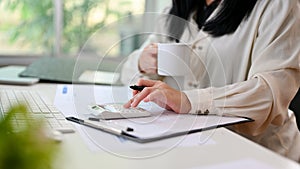 A professional Asian businesswoman using calculator, sipping coffee and working at her desk